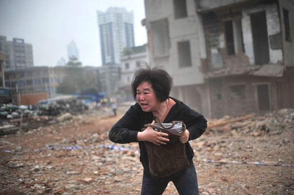 Una mujer de etnia oriental llora desconsolada  atras de ella se ven muchas casas destruidas  no vemos cual sea la causa
