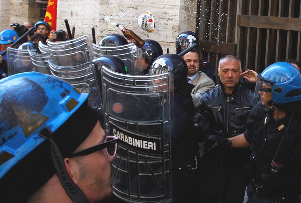 Tenemos a varios policías  protegidos con escudos deteniendo una protesta en uno de los escudos dice carabinieri 