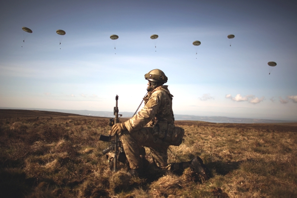 Vemos a un soldado con uniforme camuflado en un campo de entrenamiento tambien en el espacio otros soldados lanzándose en paracaídas
