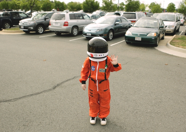 Vemos aun pequeño niño que lleva puesto un traje de astronauta en color naranja a su lado se ven varios carros