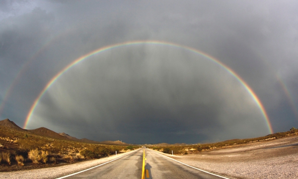 Tenemos un hermoso paisaje una carretera y al fondo un doble arco iris en sus hermosos colores en un atardecer