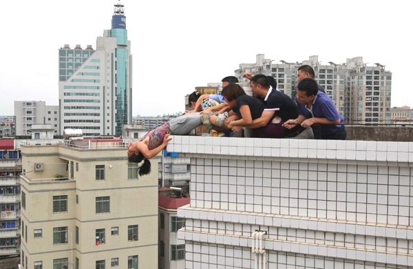 Una mujer en la terraza de un edificio es cojida de las piernas por varias personas por que  parece que quería lanzarse de allí
