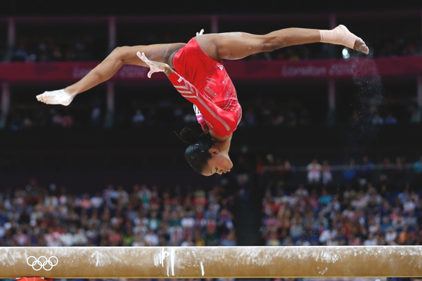 Una atleta con uniforme rojo hace un figura de salto para caer sobre  una barra