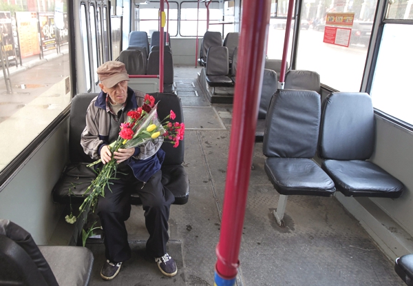 Vemos a un hombre mayor con una gorra ropa sencilla y zapatos tennis  y lleva un lindo y grande ramo de flores