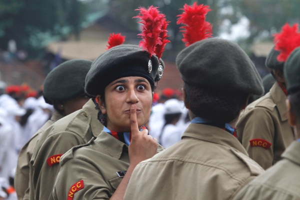 Una mujer con uniforme militar y boina hace señas a una compañera con un dedo sobre su boca para que haga silencio mientras pasa algun acto publico