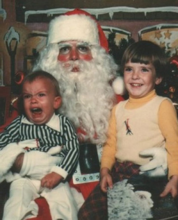 Vemos a Santa claus con dos niños uno disfruta mucho y el otro llora desconsoladamente