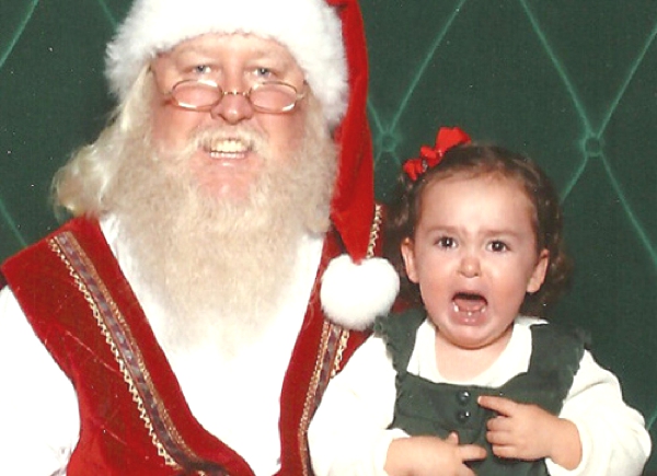 Una linda niña sentada con Santa Claus llora y no disfruta el momento con el