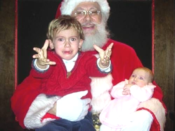 Una niña de brazos y un niño mas grandes estan sentados en las piernas de  Santa Claus y lloran amargamente