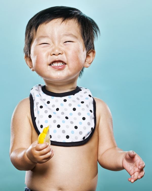 Otro pequeño niño oriental  prueba el limón y aprieta sus dientes y cierra sus ojos